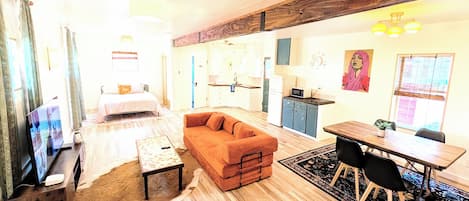 A modern living room with a sofa, a coffee table, and a TV. There is a kitchen area with cabinets and a microwave.