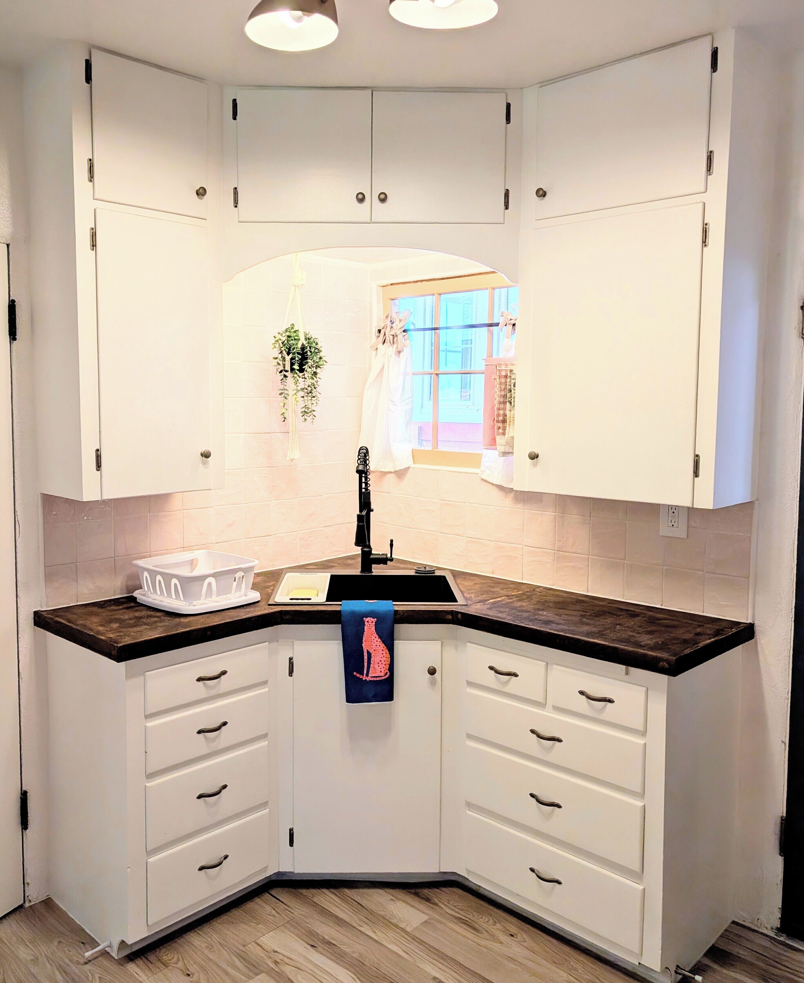 A corner kitchen with white cabinets, a black countertop, and a window with curtains.