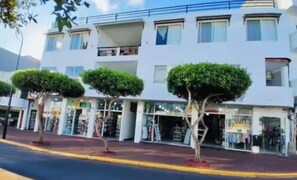 A multi-story building with a row of shops on the ground floor, a clear sky, and a street with a curb. - Downtown Apartment (Puerto Ayora)