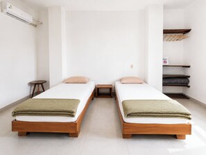 A minimalist room with two wooden beds, a small table, and a built-in shelf unit. - Downtown Apartment (Puerto Ayora)