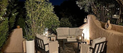 An outdoor seating area with stone flooring, a sofa, chairs, and a table.
