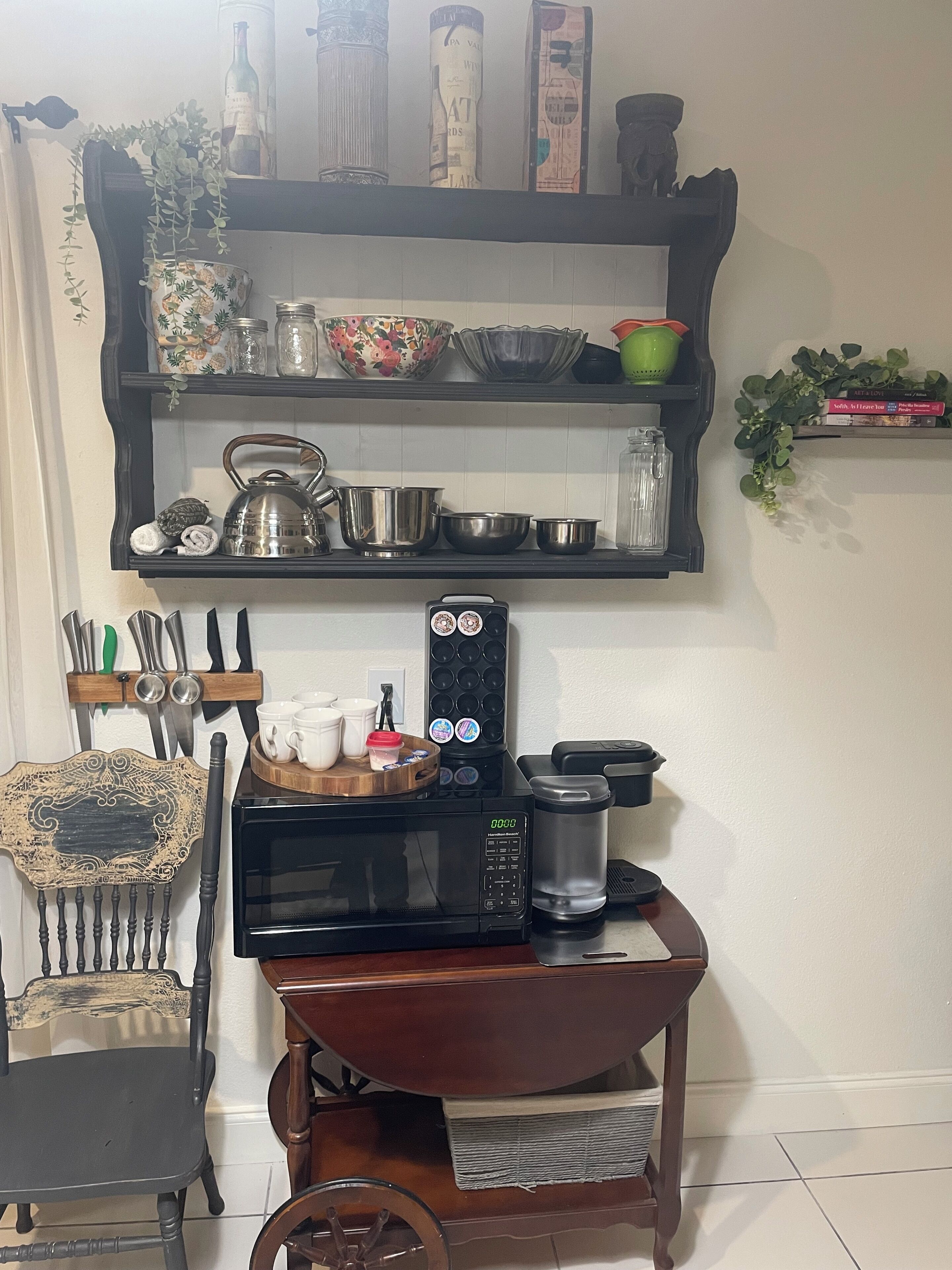 A kitchen area with a microwave, coffee maker, and various kitchen utensils on a wooden cart.