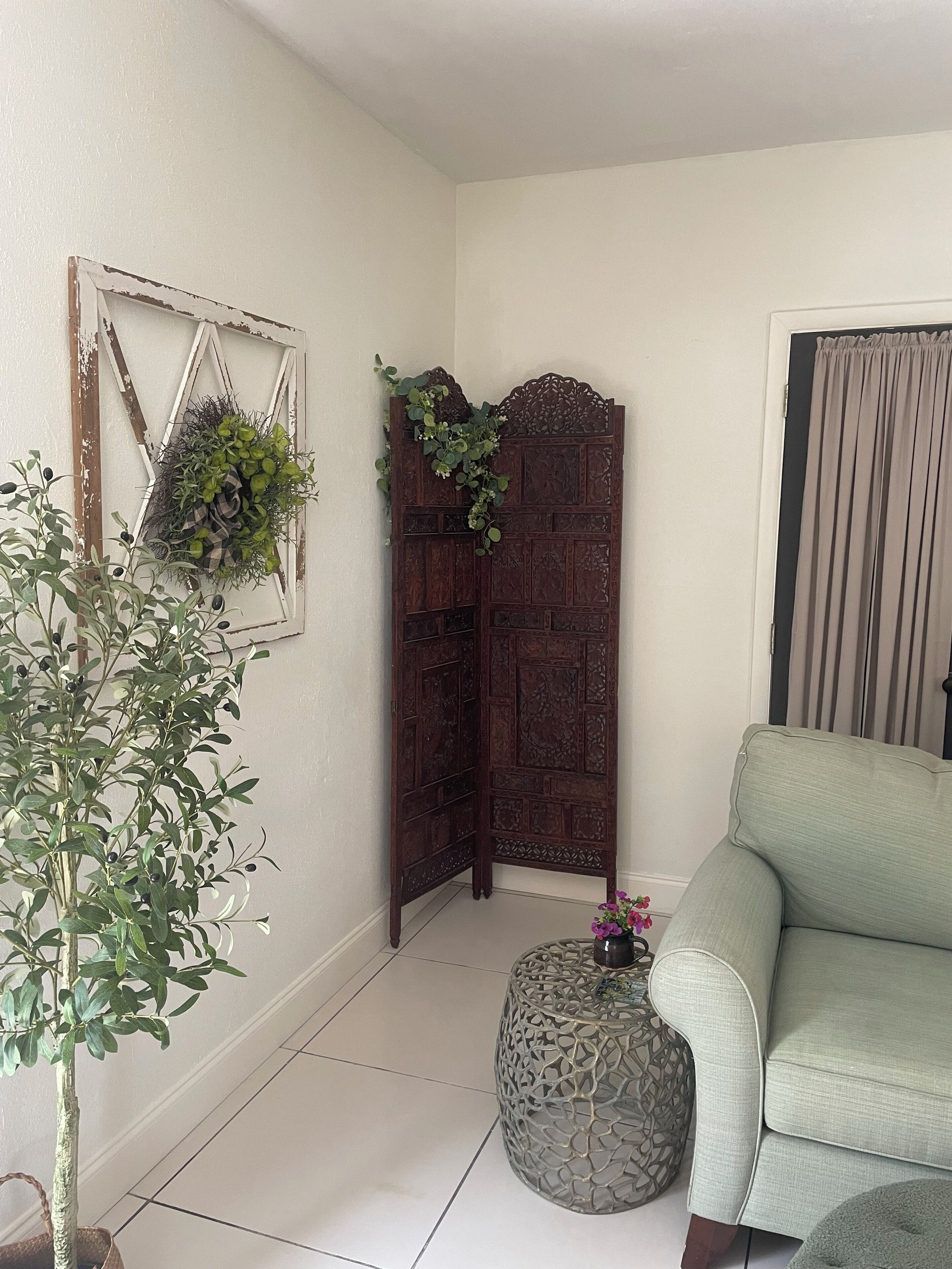 A room with a light green sofa, a decorative wooden screen, a potted plant, and a wall-mounted piece with greenery.