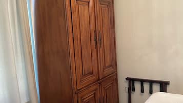A bedroom with a large wooden wardrobe, a bed with a white bedspread, and a green wicker basket.