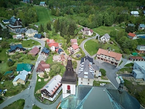 Eine Vogelperspektive eines Dorfes mit verschiedenen Gebäuden, darunter eine Kirche mit einem markanten Kirchturm, umgeben von Wohnhäusern und einem Skigebiet.