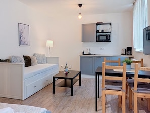 A modern living room with a sofa, a dining table with chairs, a small coffee table, and a kitchen area with a microwave and cabinets.