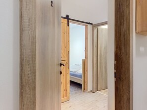 Une pièce avec un lit, un plancher en bois et une porte coulissante donnant sur une autre pièce.