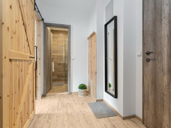 A hallway with wooden flooring, a door with a mirror, and a small plant.
