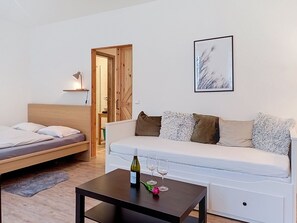 A modern bedroom with a bed, a sofa, a table with a bottle and glasses, and a framed picture on the wall.