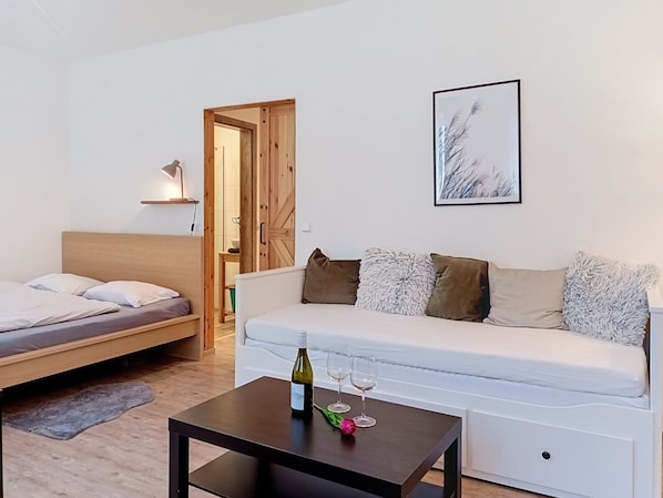 A modern bedroom with a bed, a sofa, a table with a bottle and glasses, and a framed picture on the wall.