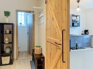 Eine moderne Küche mit Mikrowelle, Kaffeemaschine und einer Weinflasche. Eine Holztür mit Griff und ein kleiner Tisch mit einer Pflanze sind ebenfalls vorhanden.