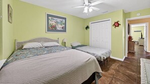 Ein Schlafzimmer mit zwei Betten, einem Deckenventilator, einer Tür mit einem dekorativen Kranz und einem Flur, der in einen weiteren Raum führt.