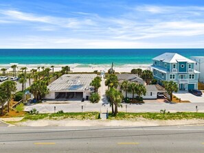 A coastal property with a parking area, a building with a flat roof, and a view of the ocean. - Steps To Beach Access 45 & Salty Goat Saloon (Panama City Beach)