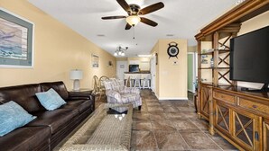 Ein Wohnzimmer mit einem braunen Ledersofa, einem gemusterten Sessel, einem gewebten Couchtisch, einer Holz-Unterhaltungsecke und einem Deckenventilator.