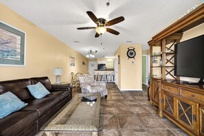 A living room with a brown leather sofa, a patterned armchair, a woven coffee table, a wooden entertainment center, and a ceiling fan. - Steps To Beach Access 45 & Salty Goat Saloon (Panama City Beach)
