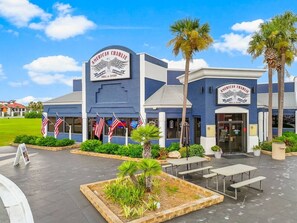 Um edifício com a placa 'American Charlie Grill & Tavern', mesas ao ar livre e bandeiras americanas.