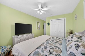 Ein Schlafzimmer mit einem Bett, einem Fernseher auf einer Kommode, einem Deckenventilator und einer Tür.