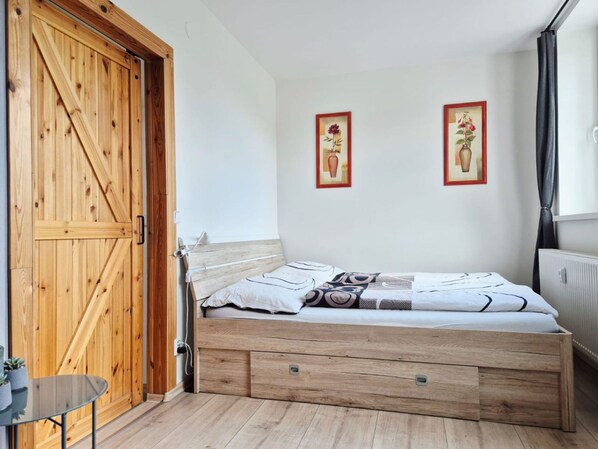 Un dormitorio con una cama de madera, una mesa de vidrio y dos cuadros en la pared.