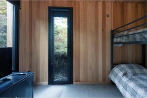 A room with a bunk bed, a door leading to an outdoor area, and a television on a cabinet.