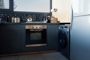 A modern kitchen with a built-in oven, a washing machine, and a window above the counter. - Wasi | Mountain Cabin with a View of Lake Lácar (San Martín de los andes)