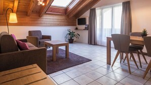 Un espacio habitable estilo loft acogedor con techo inclinado, vigas de madera, tragaluz, televisor de pantalla plana, zona de comedor y una planta en maceta.