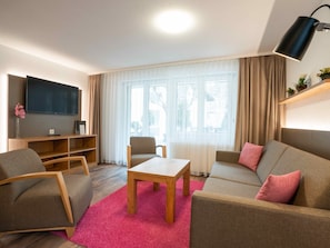 Uma sala de estar moderna com um sofá, poltronas, uma mesa de centro e uma televisão.