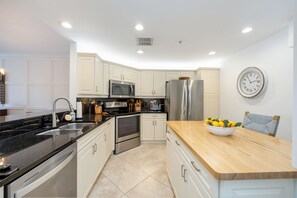 A modern kitchen with white cabinetry, stainless steel appliances, and a wooden countertop.