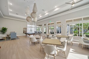 A spacious indoor area with multiple tables and chairs, a pool table, and large windows allowing natural light. - Newly Remodeled Naples Retreat - Resort-Style Living at Bridgewater Bay (Naples)