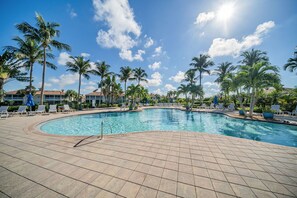 A swimming pool with a tiled deck, surrounded by palm trees and lounge chairs.