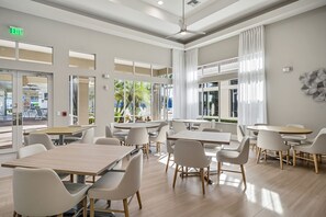 A modern dining area with multiple tables and chairs, large windows with curtains, and an exit sign.