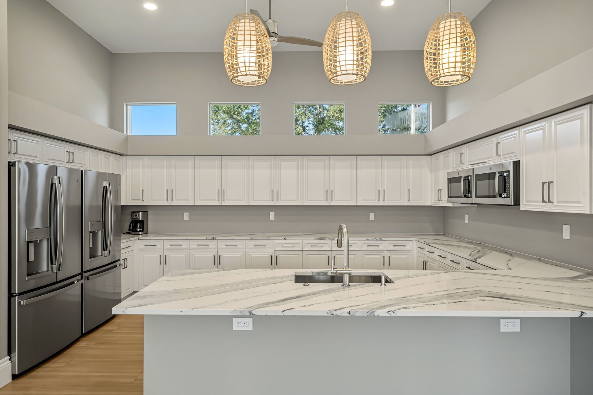 Een moderne keuken met witte kastjes, roestvrijstalen apparatuur, een marmeren eiland en hanglampen.