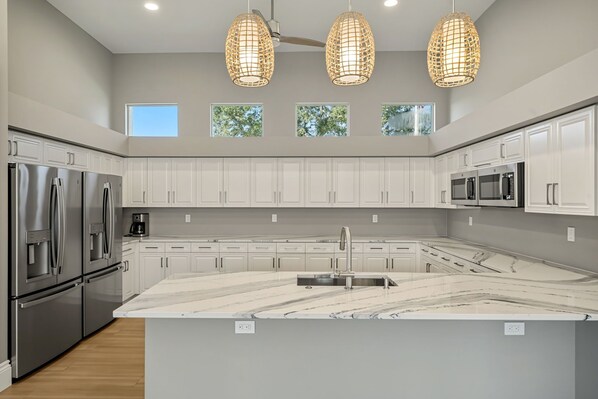 A modern kitchen with white cabinetry, stainless steel appliances, a marble island, and pendant lighting.