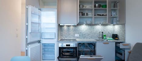 Una cocina compacta con horno integrado, lavavajillas y un refrigerador con varios compartimentos.