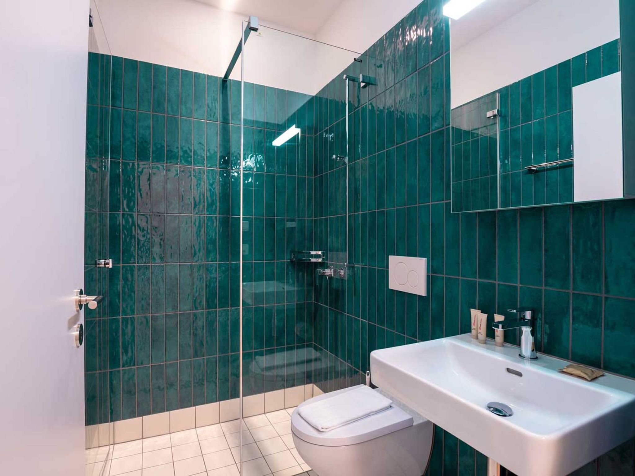 Un baño moderno con cabina de ducha de vidrio, inodoro blanco y lavabo con espejo superior.