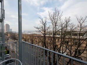 Een balkon met een metalen hekwerk dat uitkijkt over een stadsgezicht met gebouwen en kale bomen.