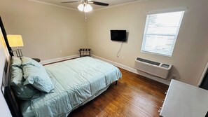 A bedroom with a bed, a ceiling fan, a wall-mounted TV, and a window with blinds.