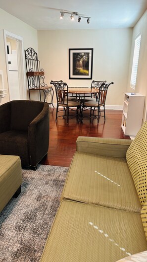 A living room with a dining table, chairs, a sofa, a bookshelf, and a framed picture on the wall.