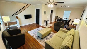 A living room with a sofa, chairs, a coffee table, a TV, and a staircase.