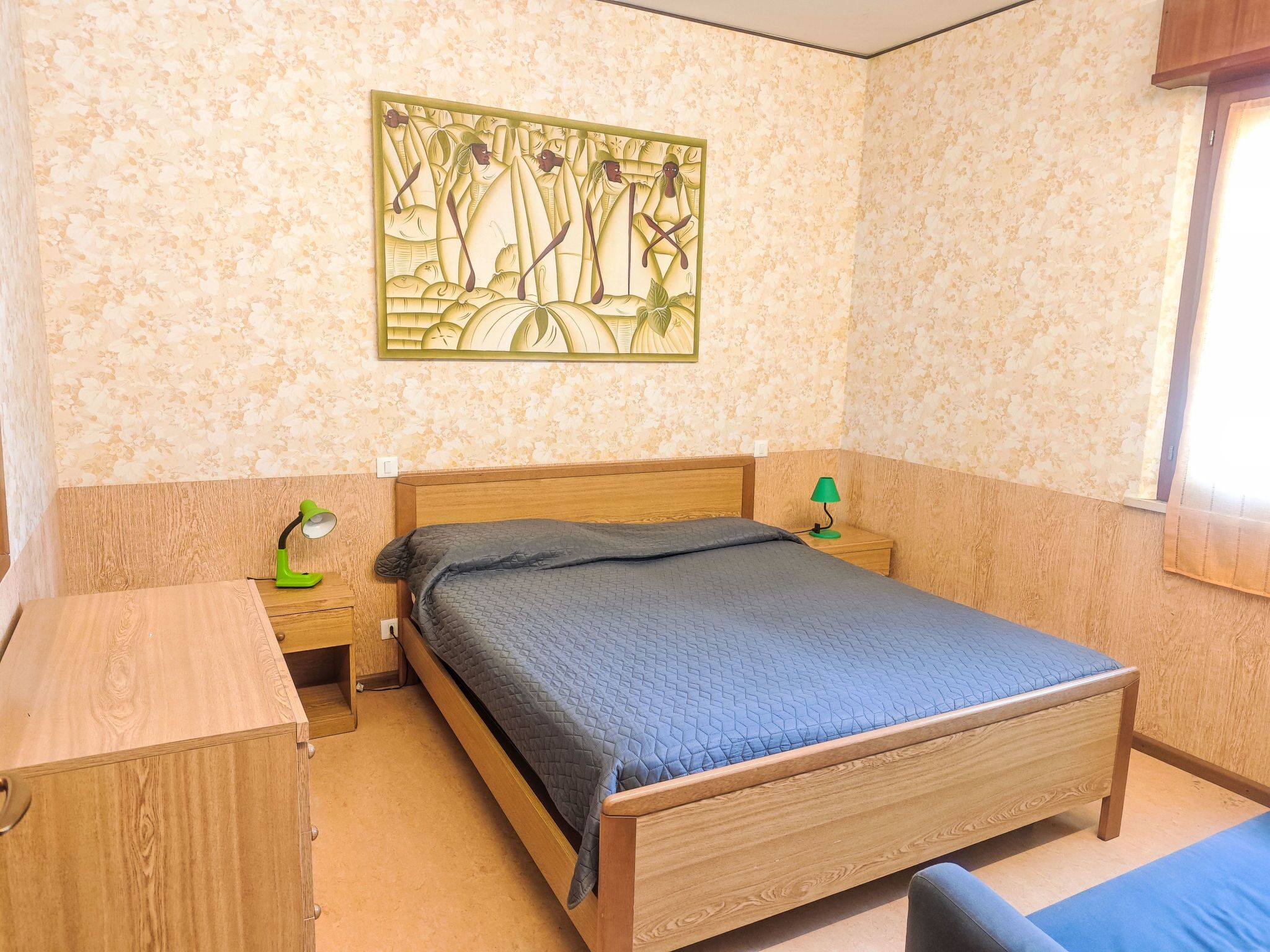 A bedroom with a wooden bed, a nightstand with a lamp, and a wall with a floral pattern.