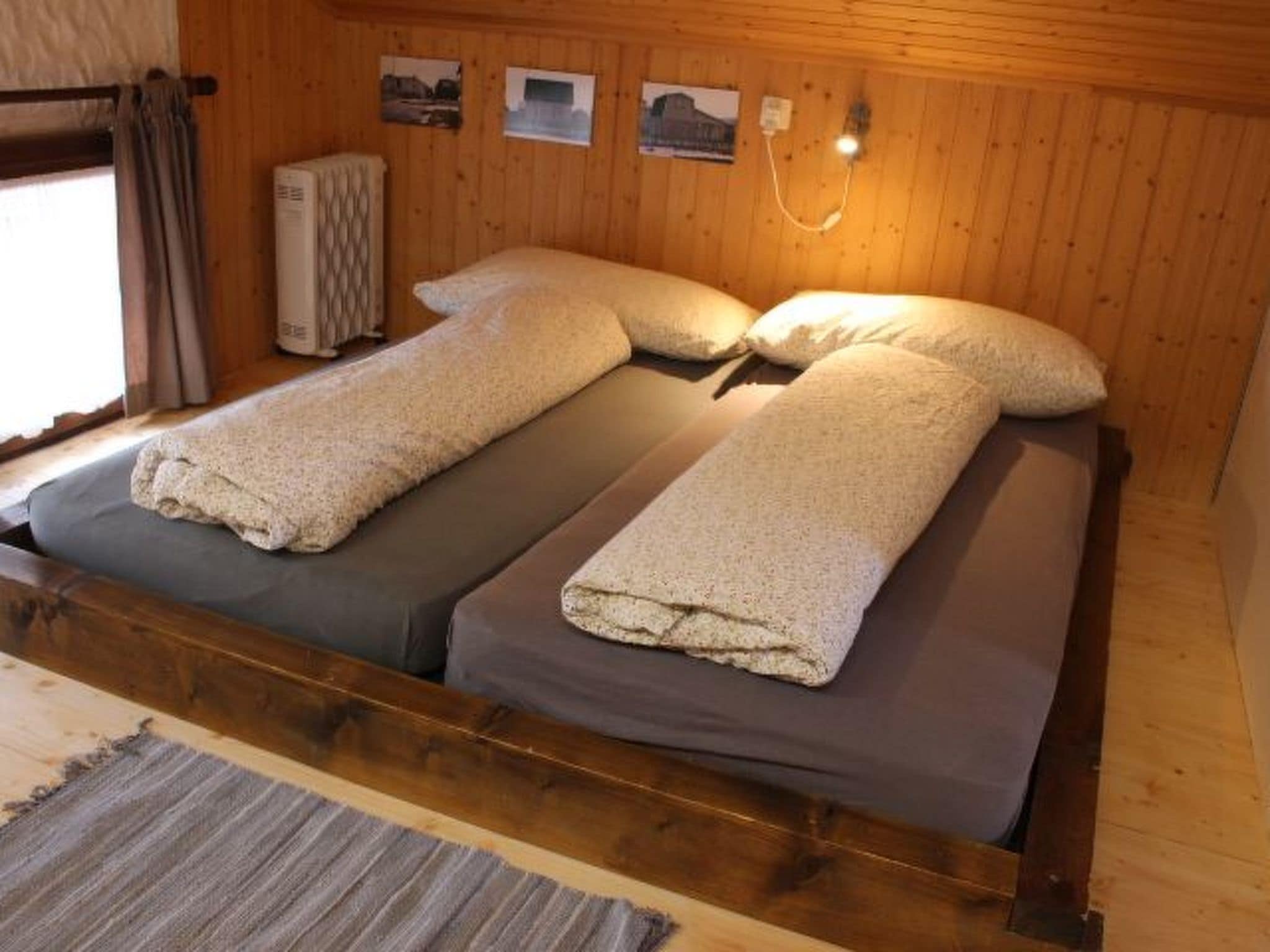 Un lit double avec deux oreillers et une couverture, des murs en bois, une fenêtre avec des rideaux et un radiateur.