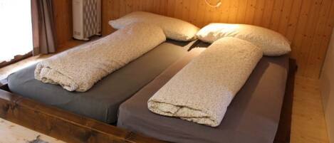 Un lit double avec deux oreillers et une couverture, des murs en bois, une fenêtre avec des rideaux et un radiateur.