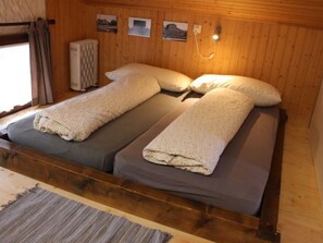 A double bed with two pillows and a blanket, wooden walls, a window with curtains, and a radiator. - Gabrielenhaus, (Wassen UR), by Interhome (Wassen UR)
