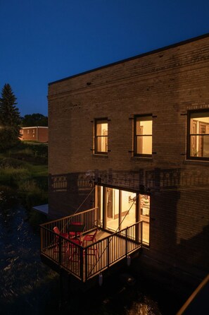 Ein Gebäude mit einer Ziegel-Fassade, einem Balkon mit roten Stühlen und einem kleinen Wasserspiegel im Vordergrund.