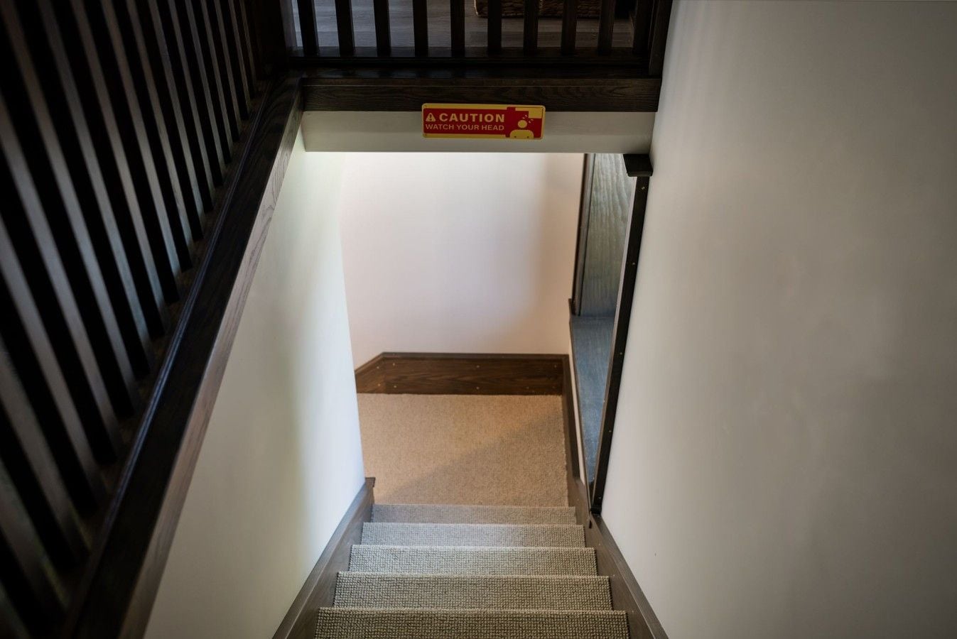 Een trap met een waarschuwingsbord, bekleed met tapijt, en een houten leuning.