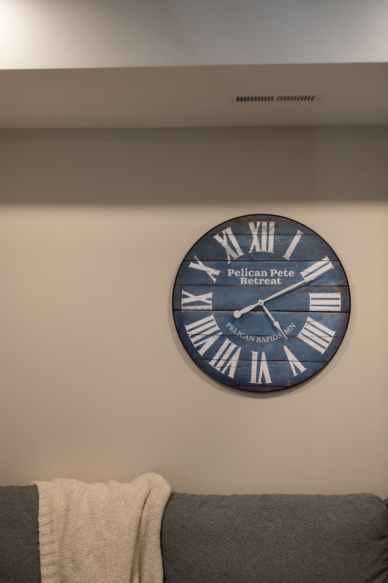 Eine runde Wanduhr mit römischen Ziffern und dem Text 'Pelican Pete Retreat' sowie 'Pelican Rapids MN'.