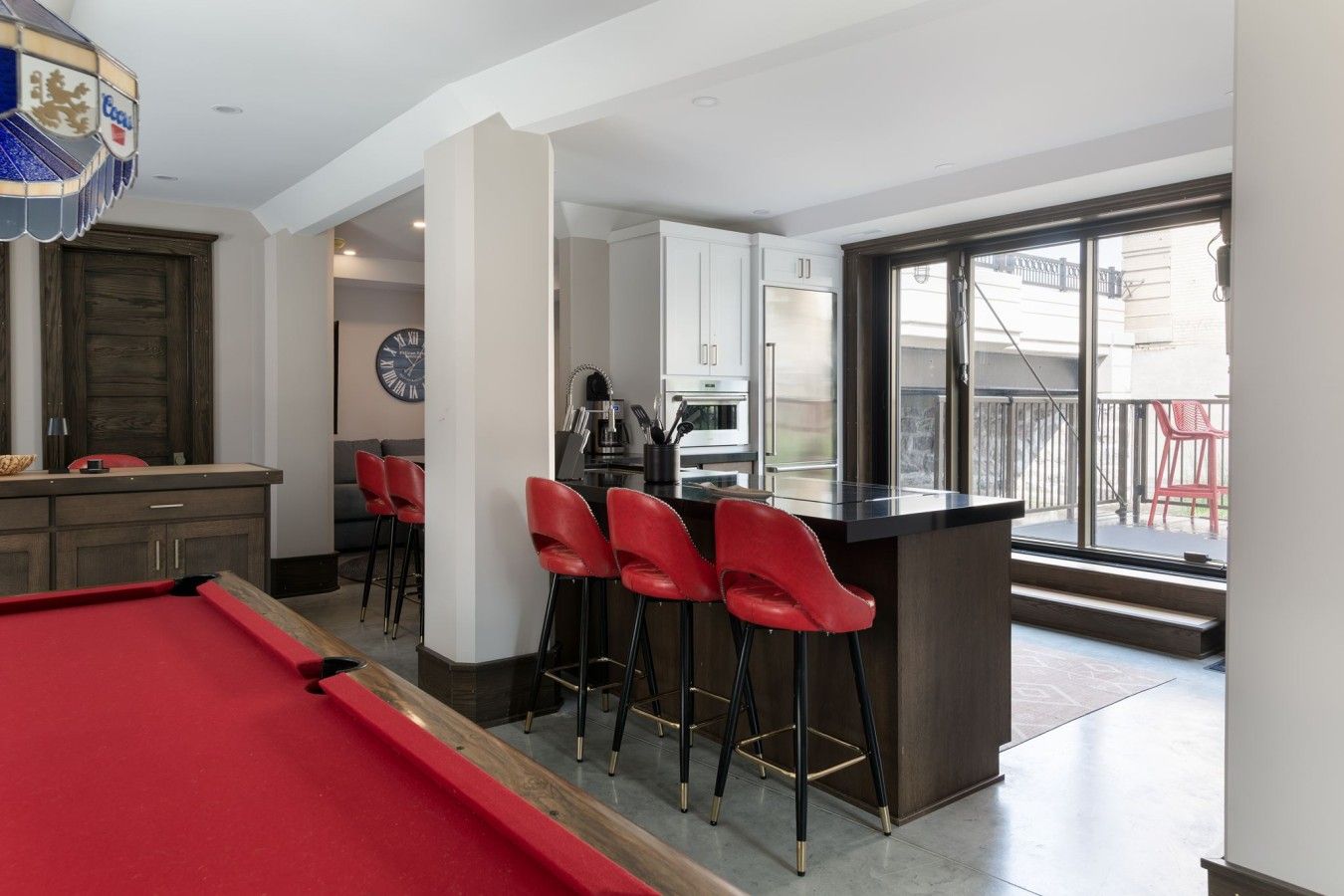 Una cocina moderna con barra, mesa de billar y comedor con sillas rojas.