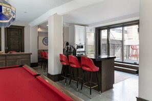 Une cuisine moderne avec un coin bar, une table de billard et un espace repas avec des chaises rouges.