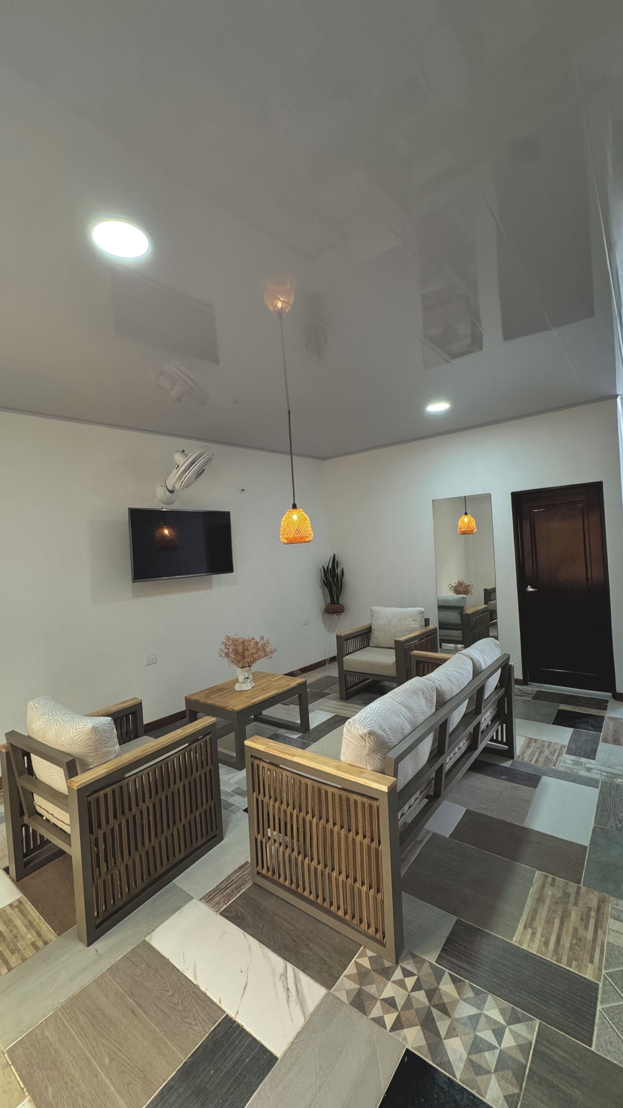 A modern living room with a sofa set, a coffee table, a TV mounted on the wall, and a patterned floor.