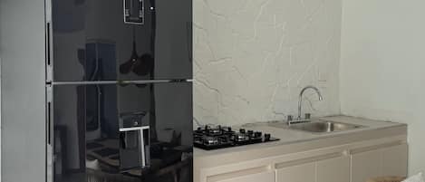 Una cocina compacta con refrigerador integrado, estufa a gas, lavamanos y un comedor con una silla.