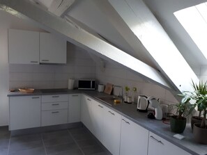 A modern kitchen with white cabinets, a microwave, a kettle, and a potted plant.